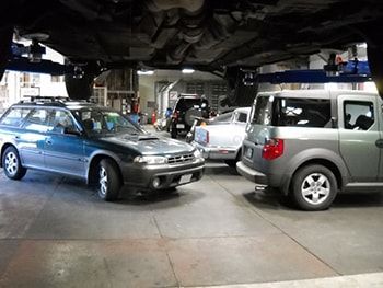 Cars parked inside a vehicle service garage with one car lifted on a hoist | Marin Automotive