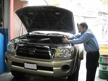 Man working under the hood of a silver SUV in a garage | Marin Automotive