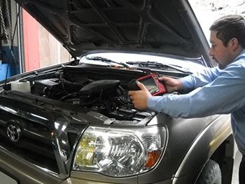 Mechanic working under the hood of a black Toyota with the hood open | Marin Automotive