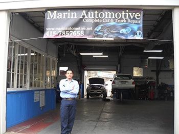 Automotive repair shop with a man standing in the entrance and vehicles inside | Marin Automotive