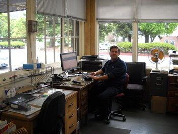 Person seated at a desk in a bright office with computers, papers, and a fan by the window | Marin Automotive