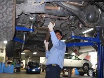 Mechanic working under a lifted car in an auto repair shop, with other vehicles in the background | Marin Automotive