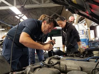 Two mechanics inspecting an engine under a lifted car in a garage | Marin Automotive