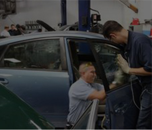 Mechanics inspecting a blue car in a garage, with one working under the open door.