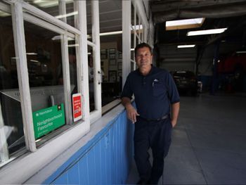 Man standing by a blue and white storefront window in a shaded walkway | Marin Automotive