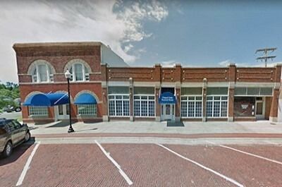 Brick storefronts with blue awnings and parked cars along a small-town street