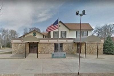 Small brick public building with an American flag, viewed from the front under a cloudy sky.