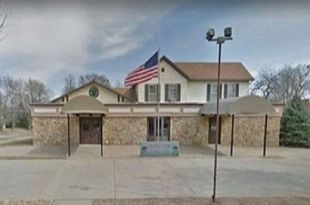 Small brick public building with an American flag, viewed from the front under a cloudy sky.