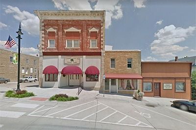 Small downtown brick storefronts with red awnings and empty parking spaces on a sunny street.