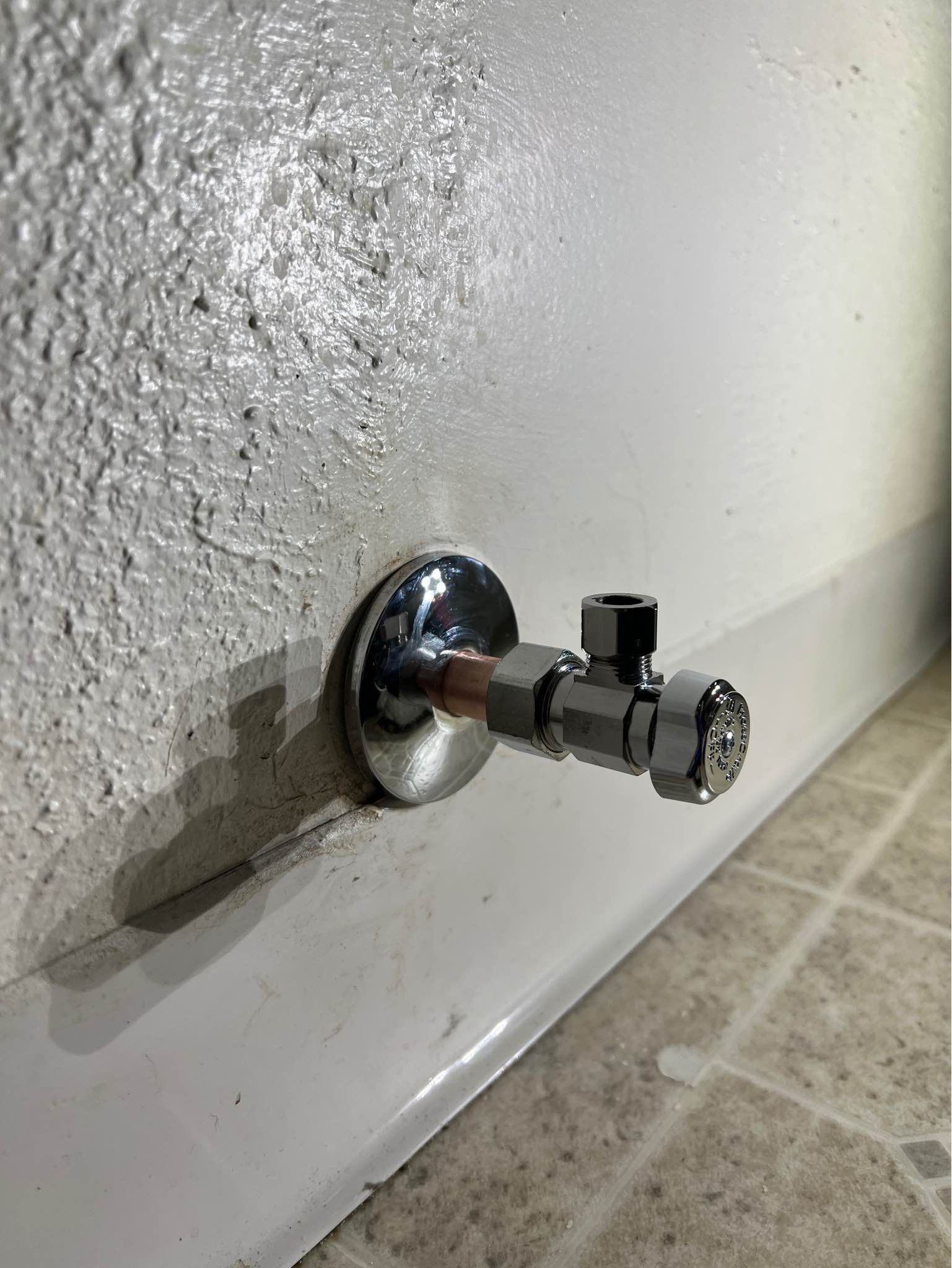 A close up of a valve attached to a wall in a bathroom.