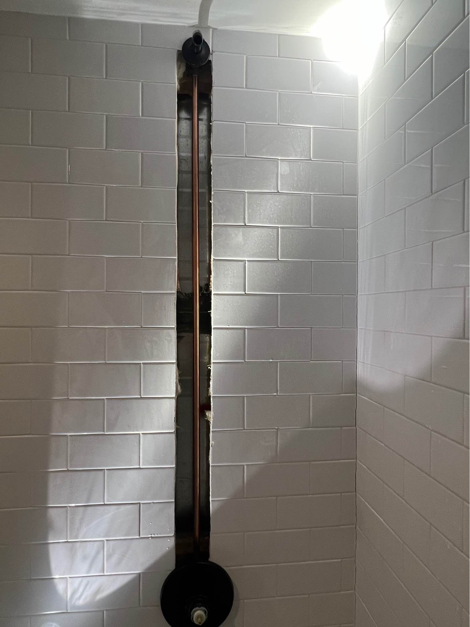 A shower head is hanging from the ceiling in a bathroom with white tiles.