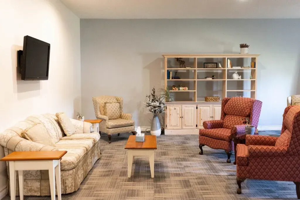 Bright living room with beige sofa, wall-mounted TV, red armchairs, coffee table, and white cabinet in back.
