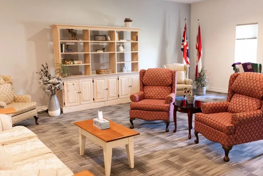 Living room with patterned chairs, sofa, coffee table, rug, cabinet, and flags near a window.