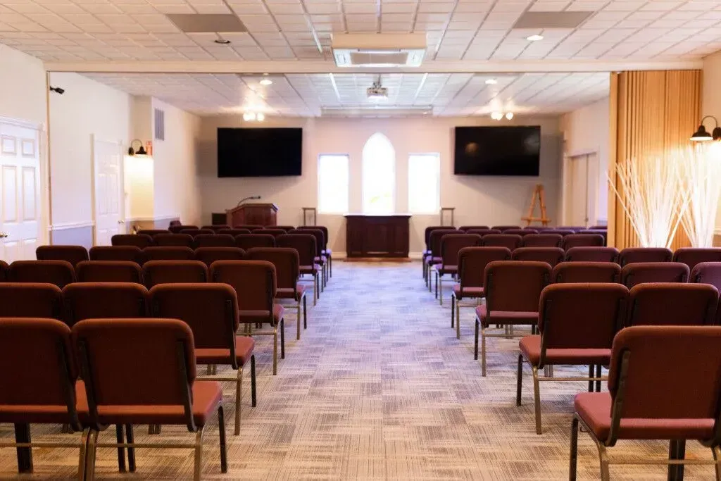 Empty conference room with rows of brown chairs facing a wall-mounted TV and podium area