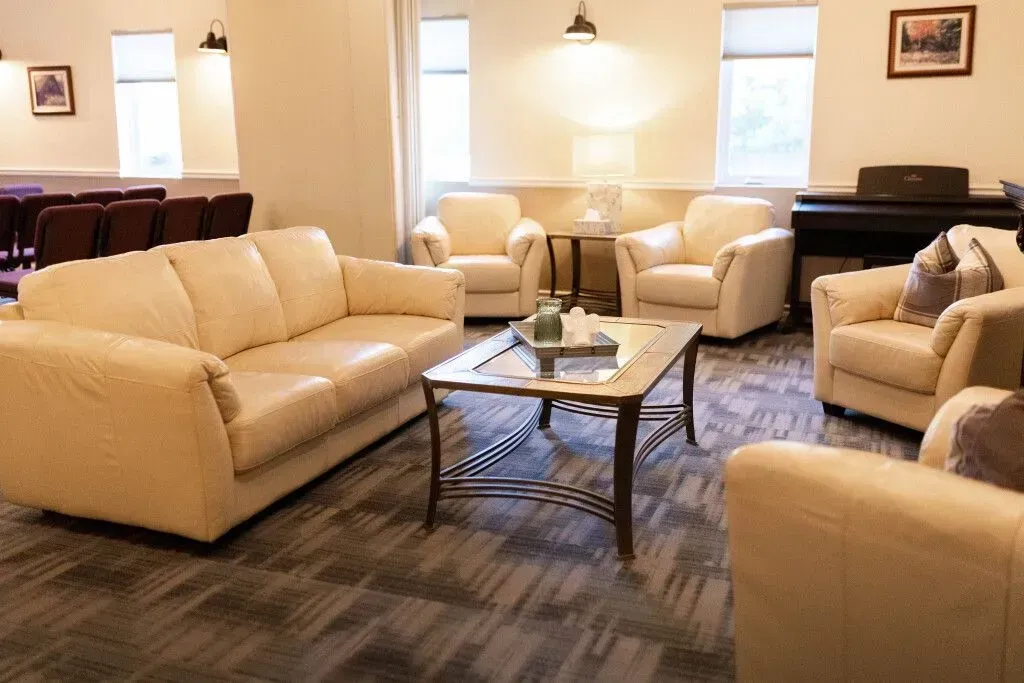 Bright living room with beige sofas, armchairs, and a glass coffee table on a patterned rug.