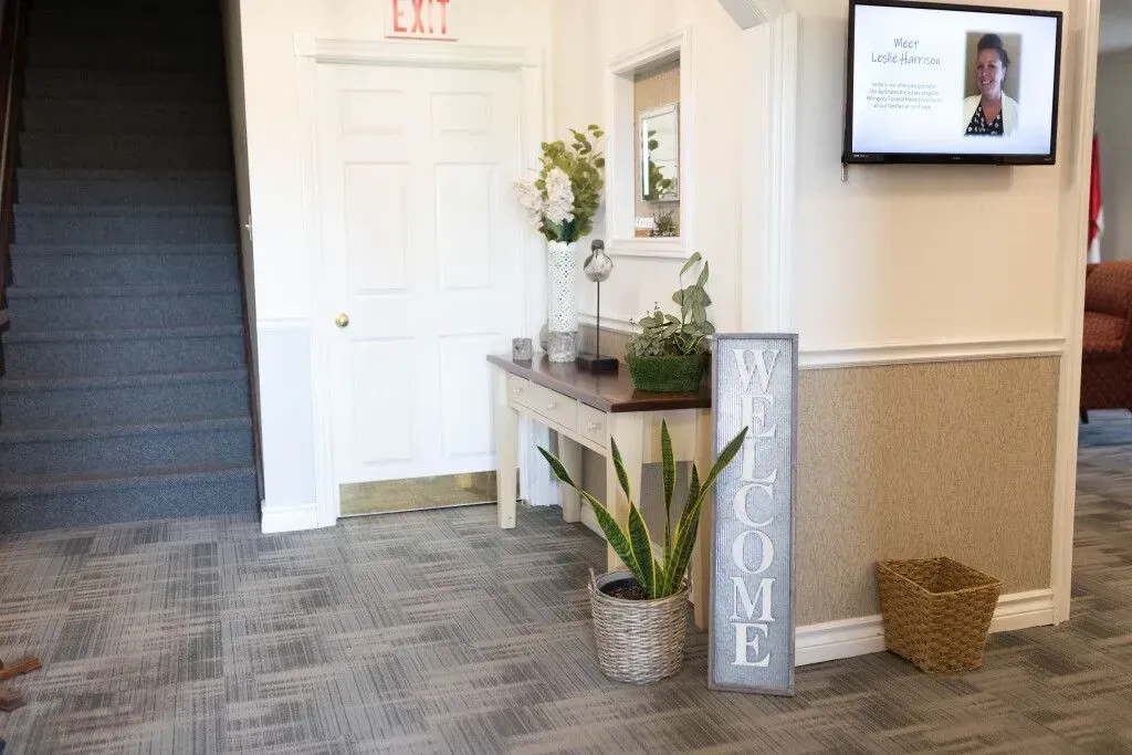 Hallway with stairs, white door, decorated table, plants, and a vertical “HOME” sign by a wall-mounted screen