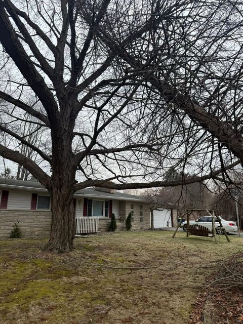 Leafless trees in front of a small house with a garage and yard in winter
