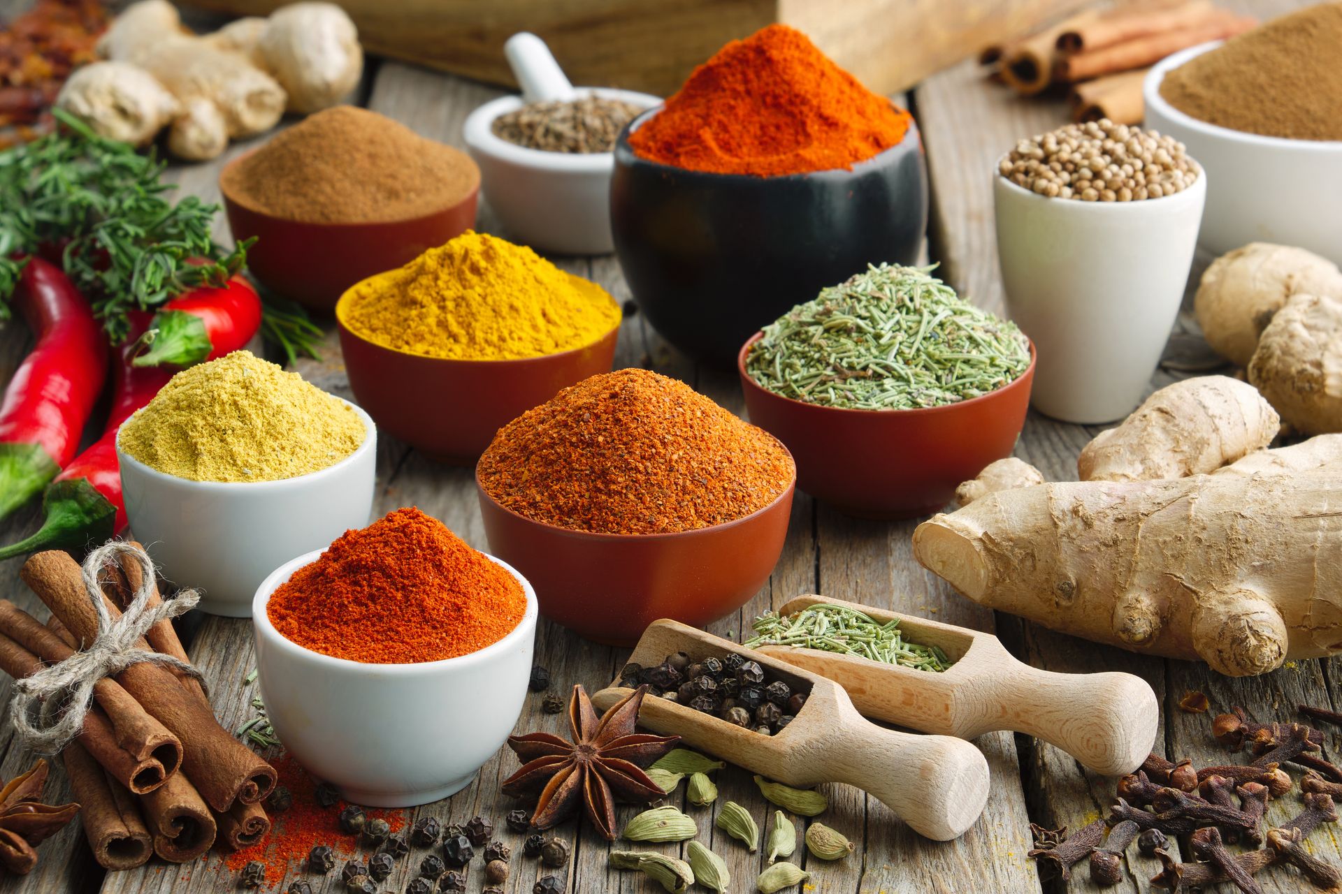 Bowls of spices: paprika, turmeric, cinnamon, ginger, cardamom, and pepper arranged on wood.