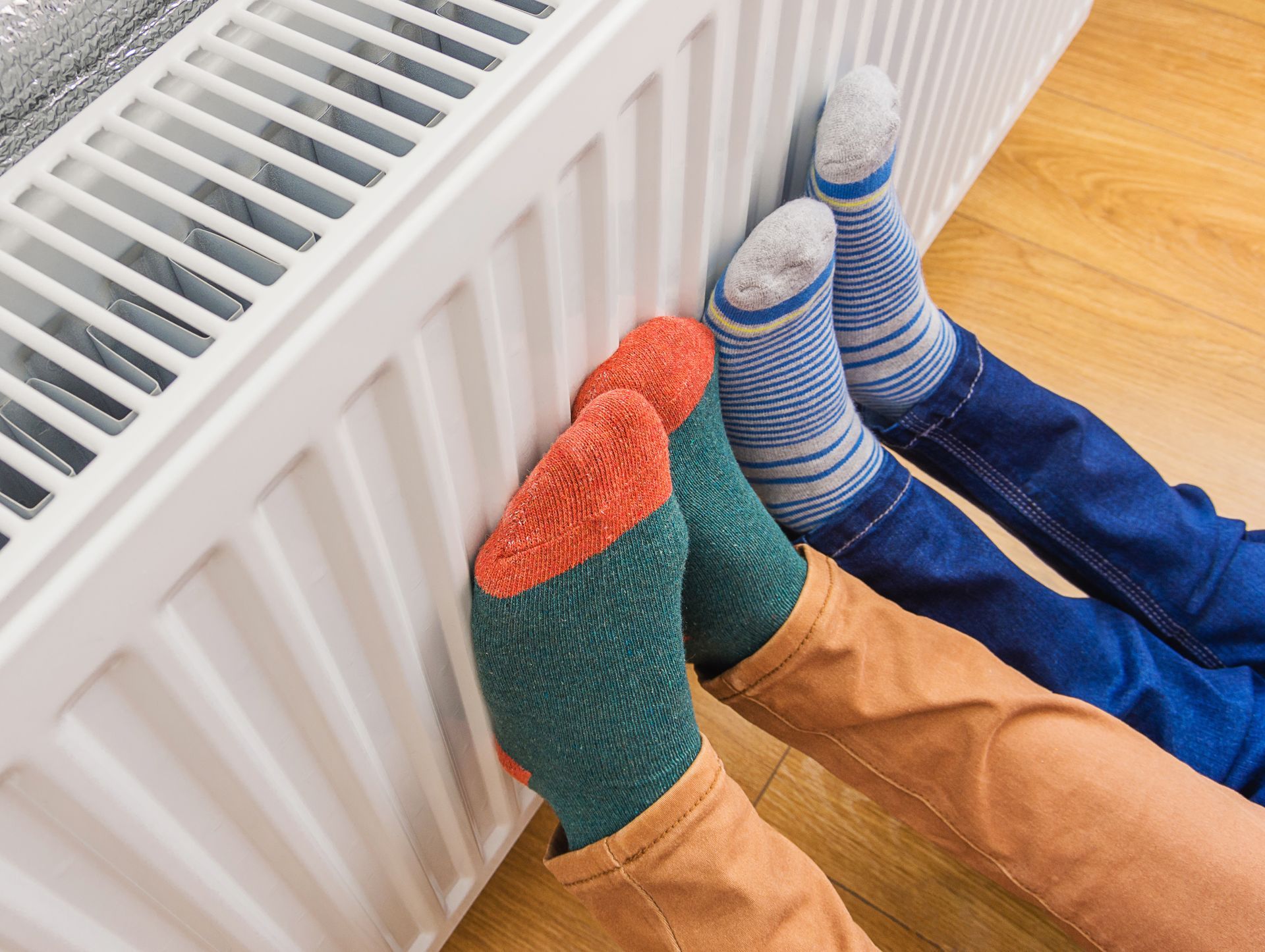 Woman and child warming cold feet at a home heating radiator in winter.