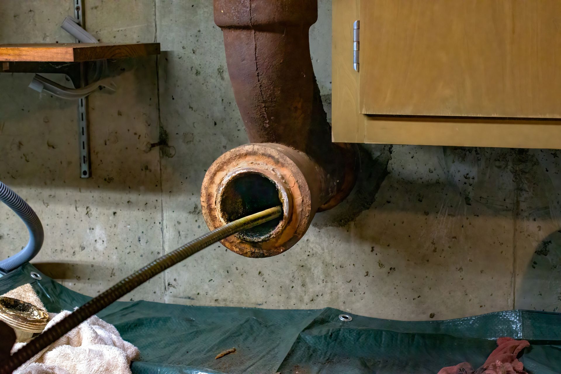 Cable auger clearing a clog from a corroded cast-iron drain pipe during drain cleaning service Cable auger clearing a clog from a corroded cast-iron drain pipe during drain cleaning service