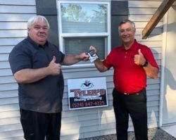 Two men are standing in front of a house giving a thumbs up.