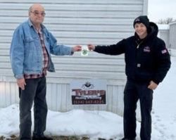 Two men are standing next to each other in front of a mobile home in the snow.