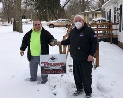 Two men wearing masks are standing in the snow holding a sign.