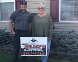 A man and a woman are standing in front of a house holding a sign.