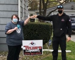 A man and a woman wearing masks are shaking hands in front of a house.