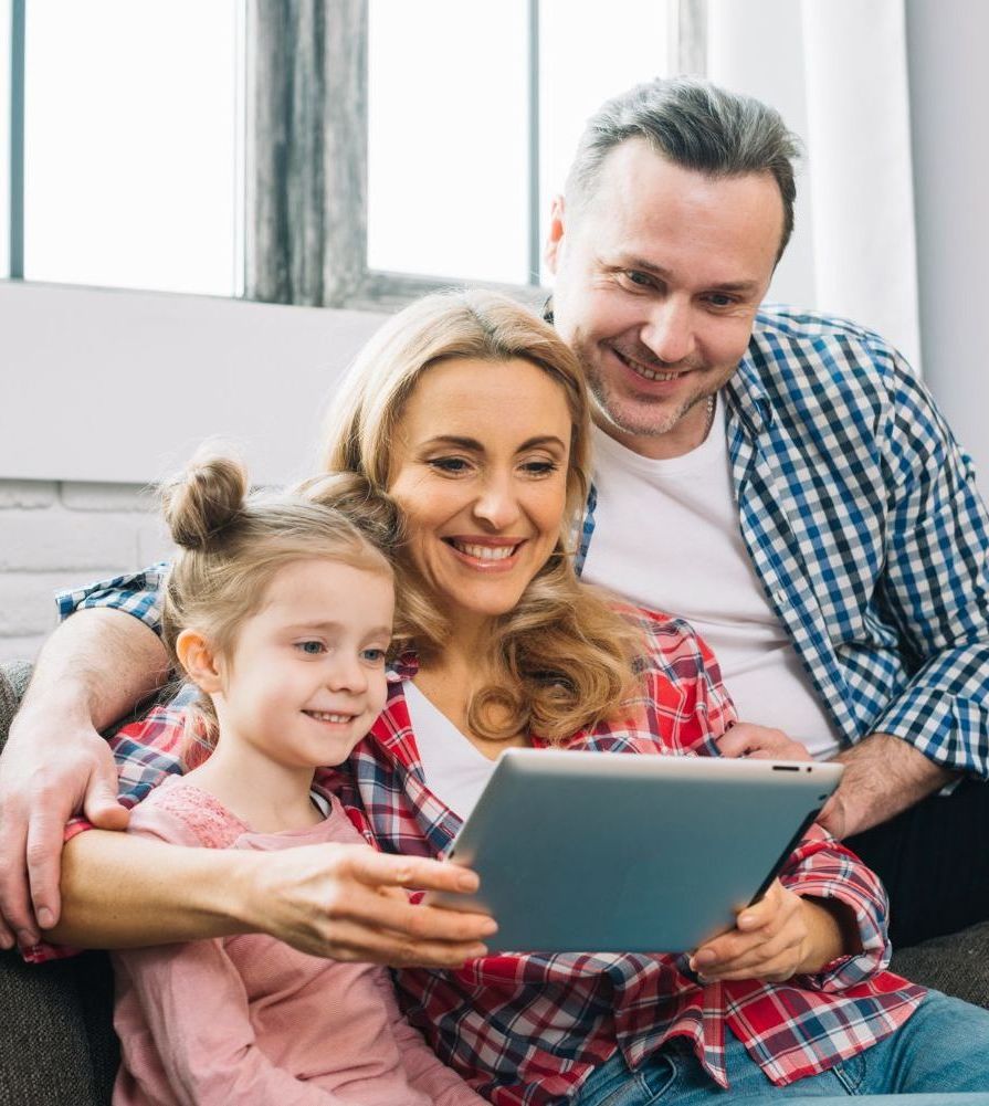 A family is sitting on a couch looking at a tablet.