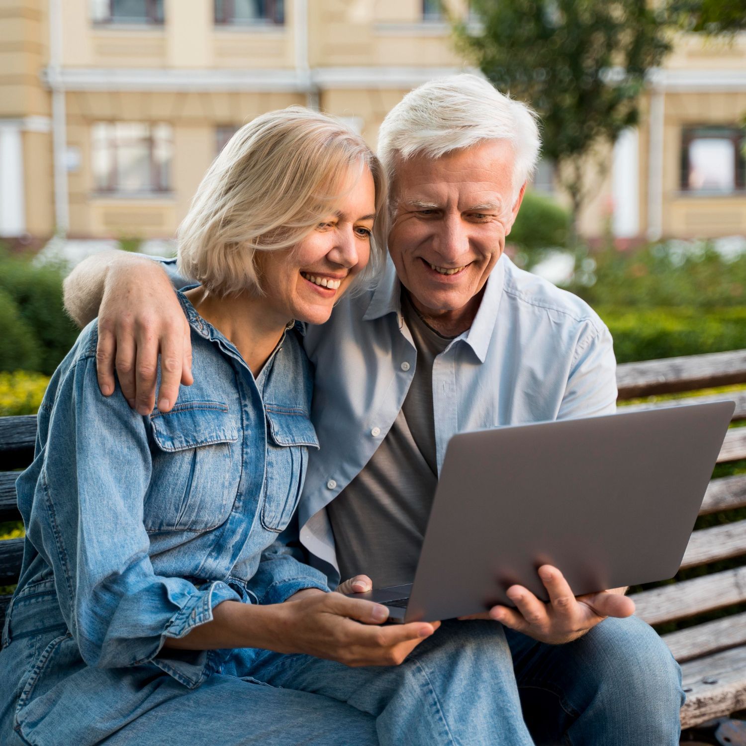 A man and a woman are sitting on a bench looking at a laptop.