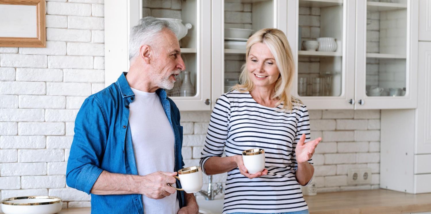 A man and a woman are standing in a kitchen holding cups of coffee.