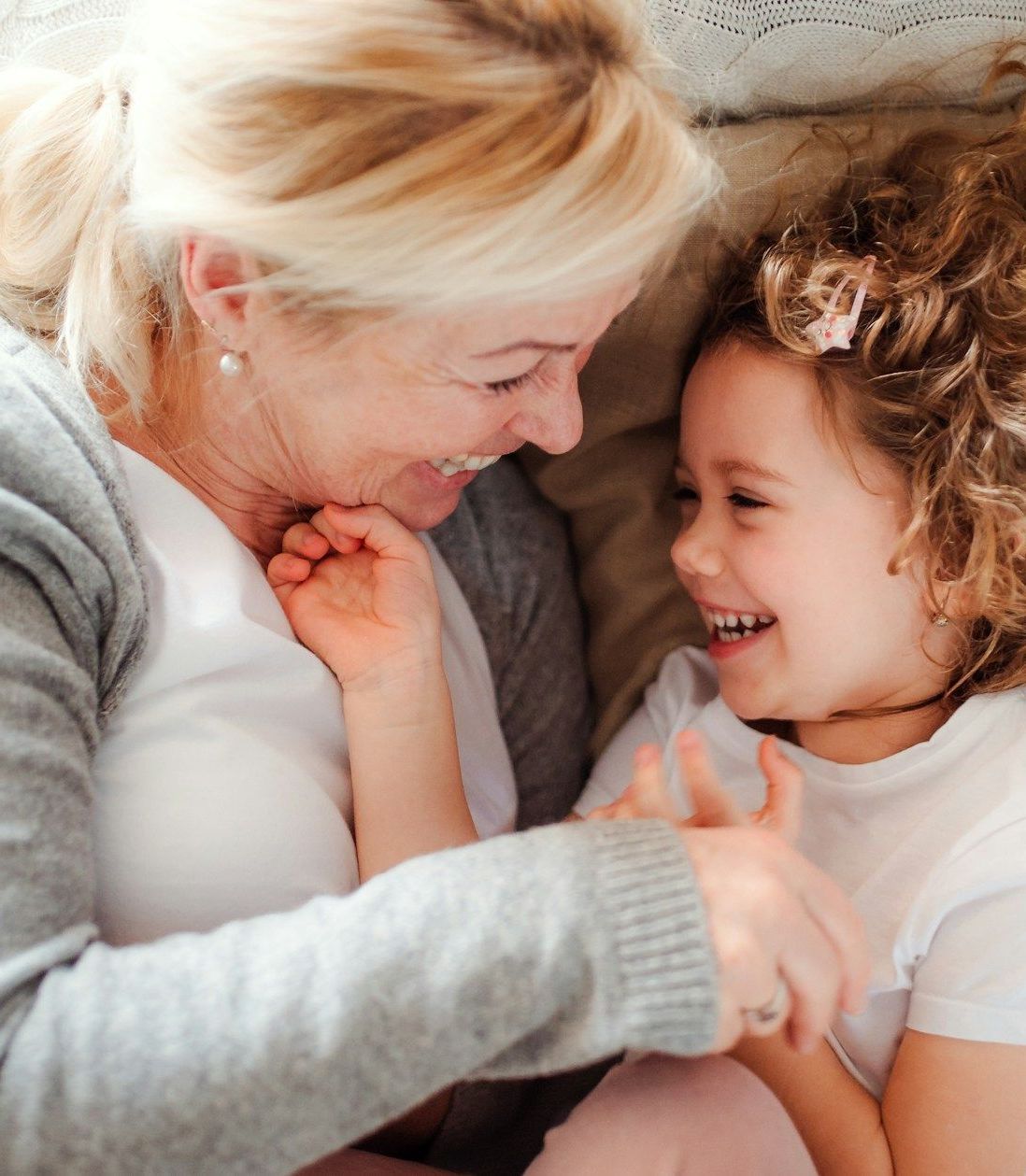 A woman and a little girl are laying on a couch holding hands and smiling.