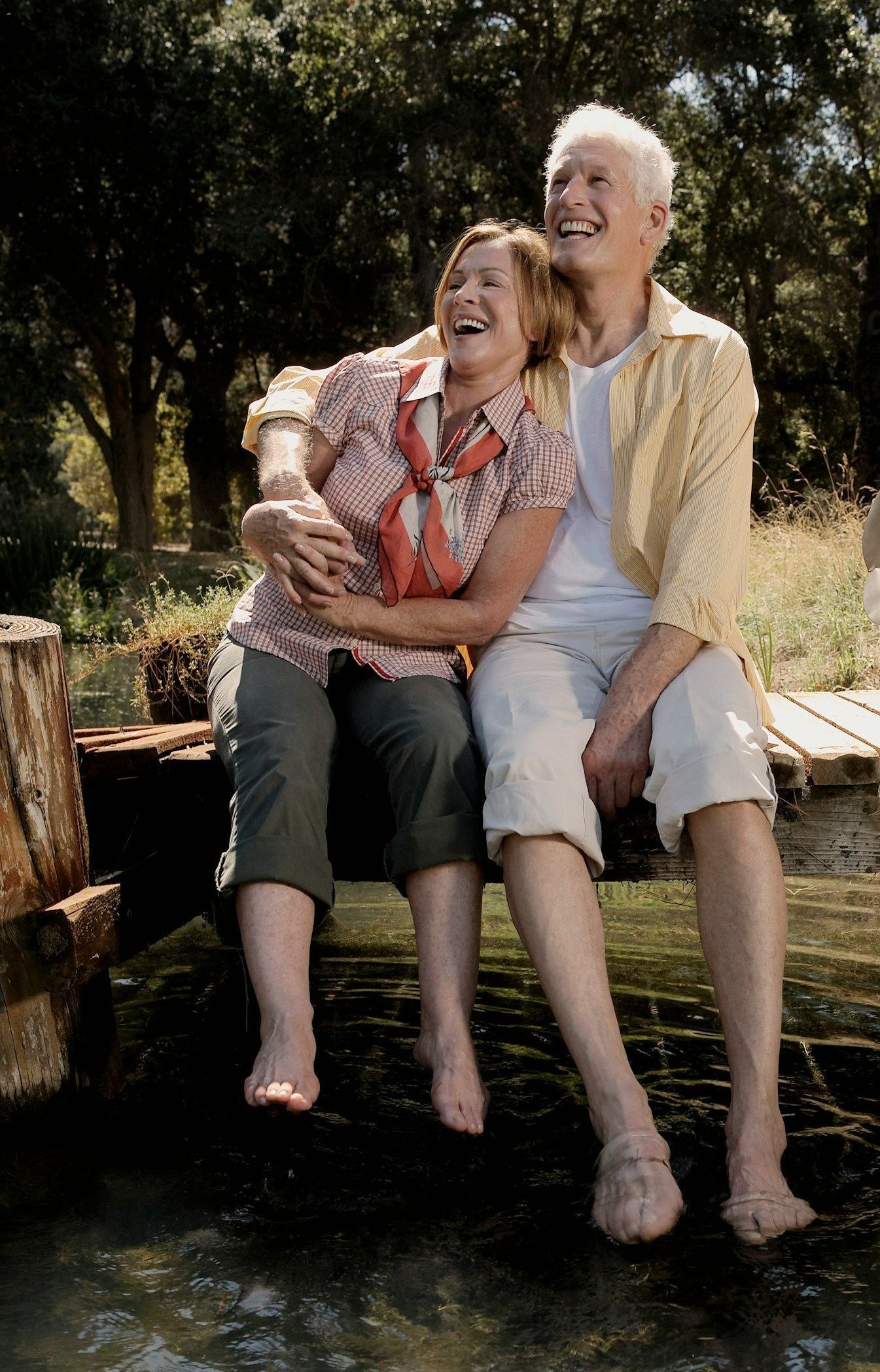 A man and a woman are sitting on a bridge over a body of water laughing.