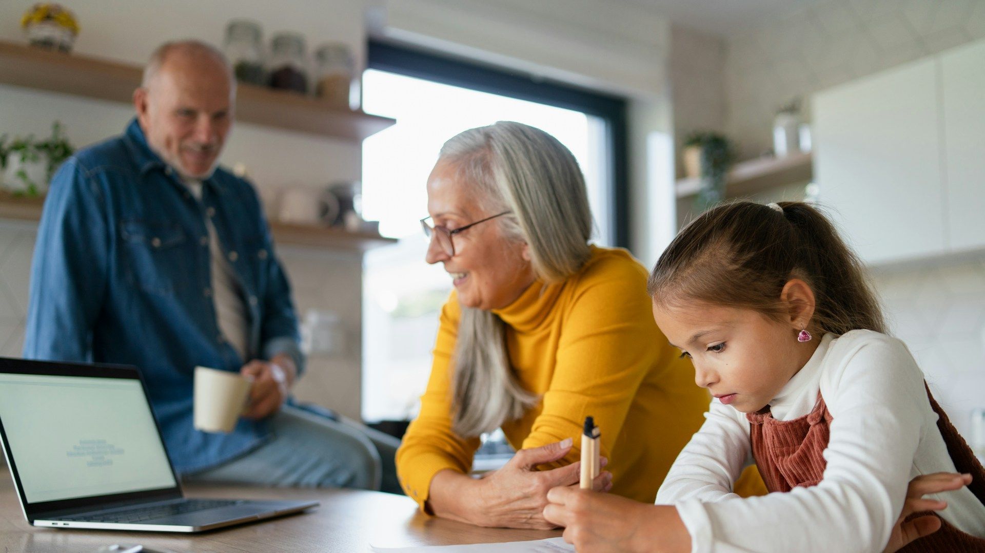 An elderly couple and a little girl are sitting at a table with a laptop.