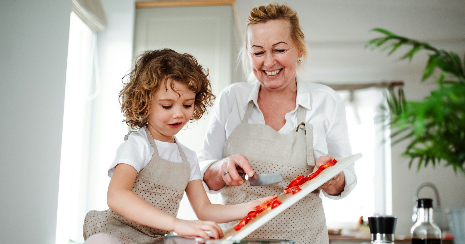 A woman and a little girl are cutting tomatoes in a kitchen.