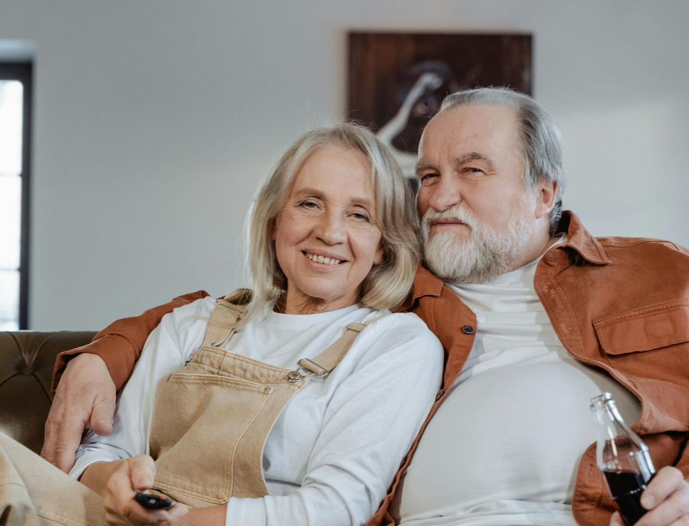 An elderly couple is sitting on a couch watching tv.