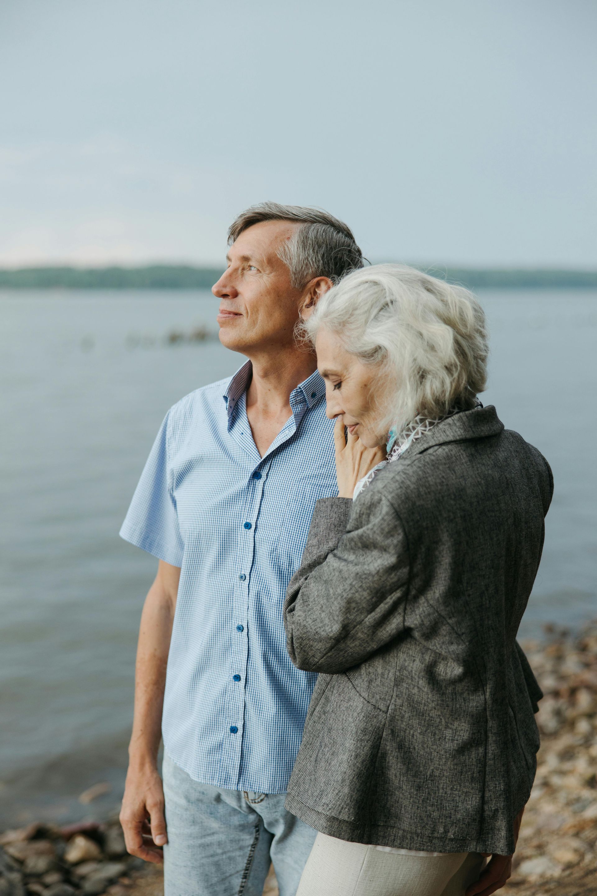 An elderly couple standing next to each other on the shore of a lake.