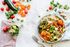 Overhead view of a colorful vegetable salad with avocado, lime, and carrots on a white table