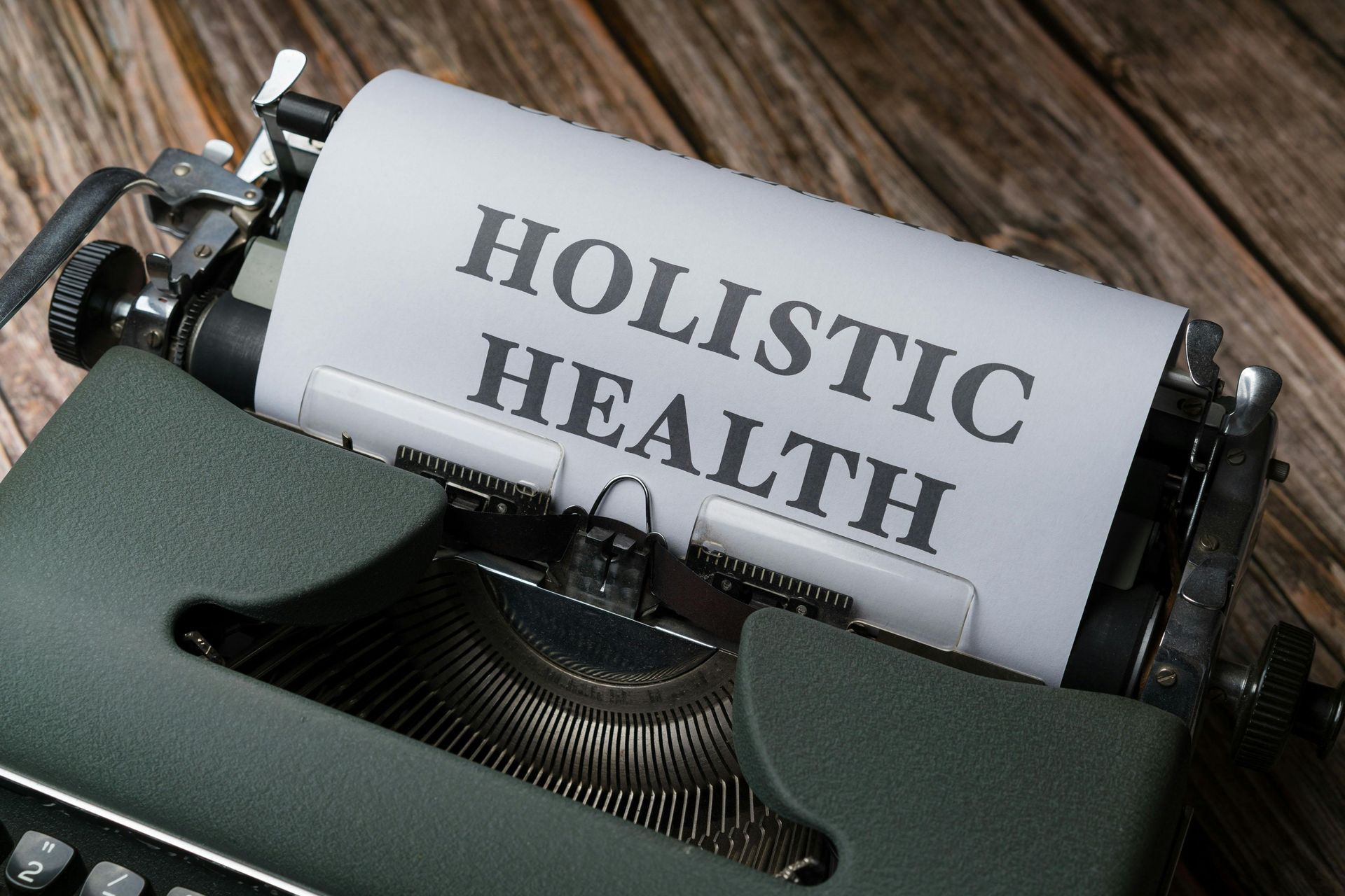 Typewriter with paper reading “HOLISTIC HEALTH” on a wooden surface.
