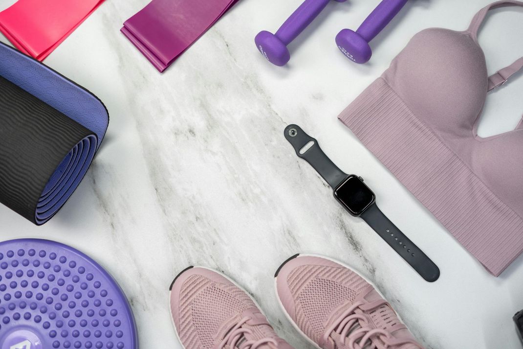 Fitness gear arranged on a marble background: yoga mat, weights, watch, shoes, and sports clothing.