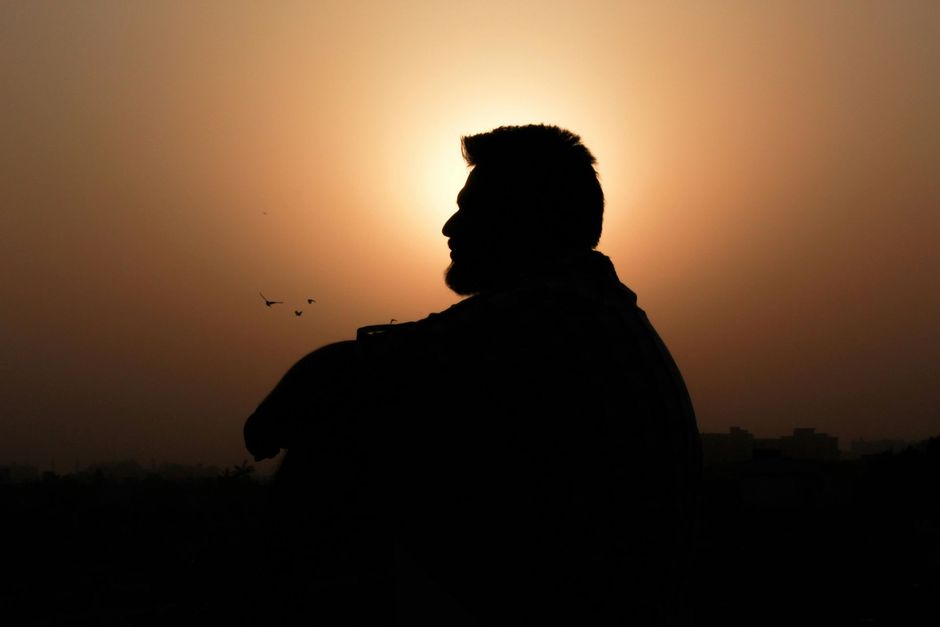 Silhouette of a person against a glowing sunset sky with birds in the distance
