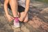 Person tying pink shoelaces on a gray sneaker while sitting on a brick sidewalk