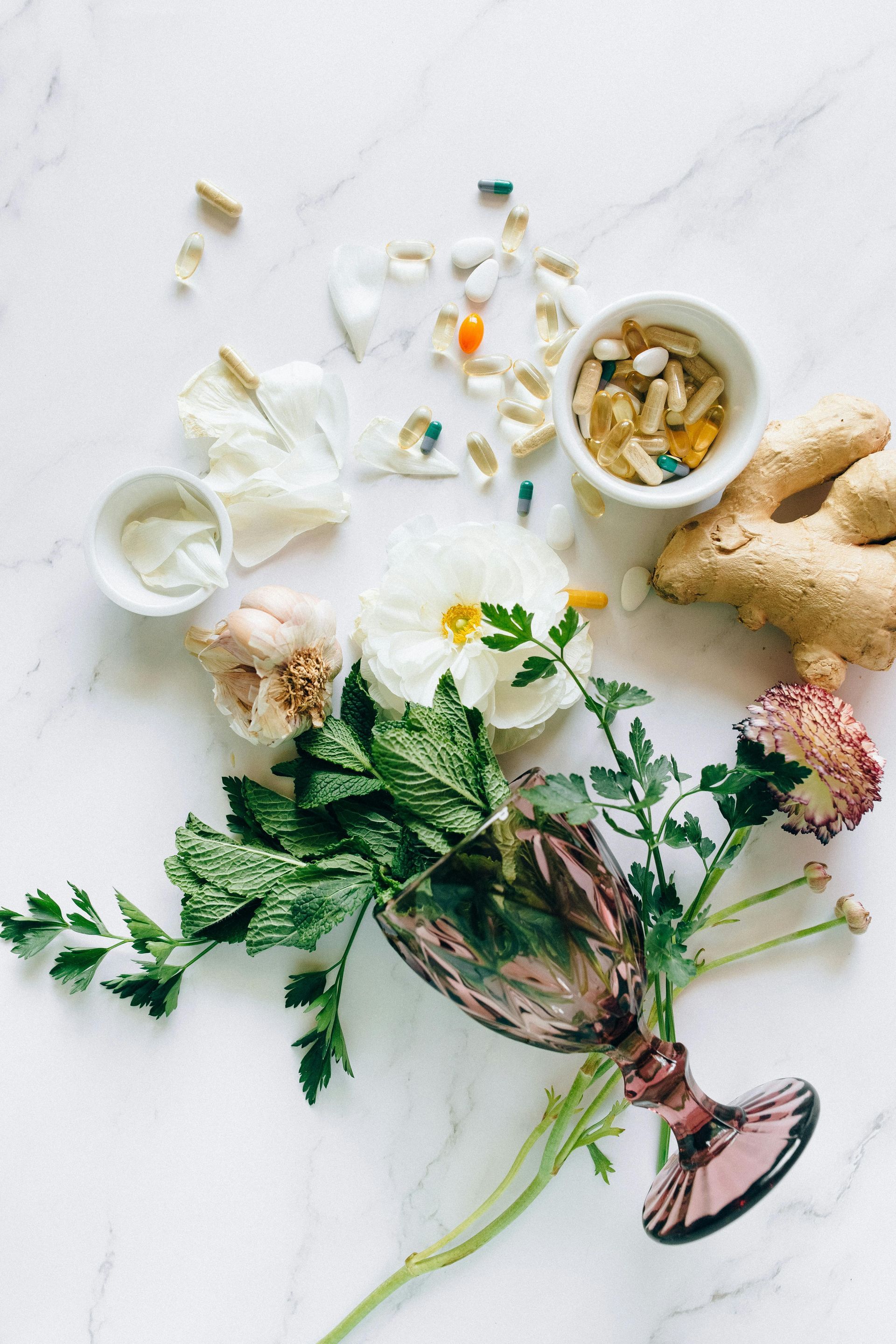Herbal tea ingredients on a white surface with mint, flowers, lemon, cups, and a teapot