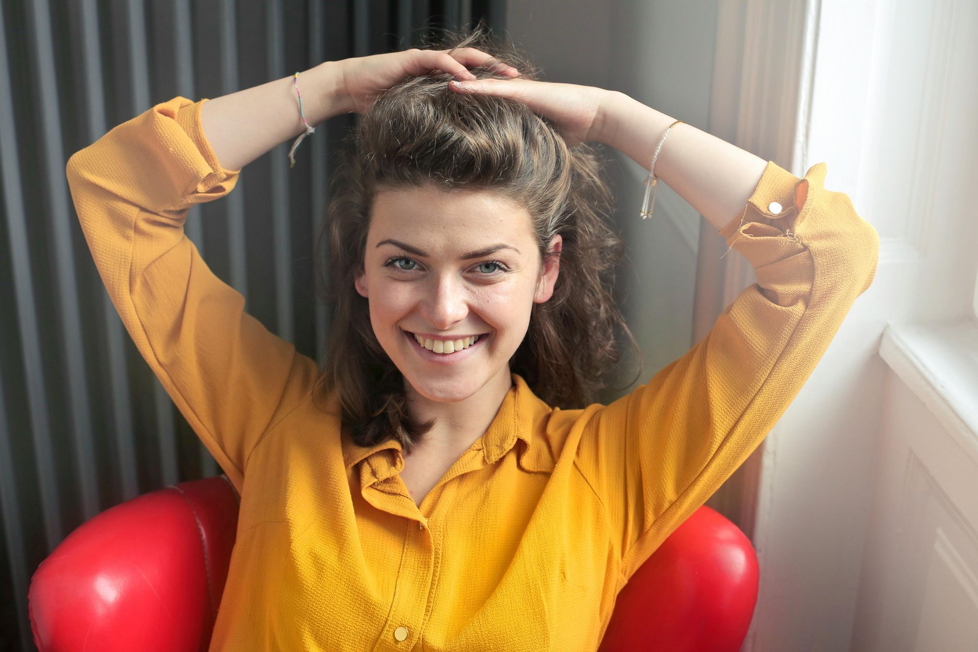 Smiling woman in a yellow shirt sitting in a red chair with arms raised overhead