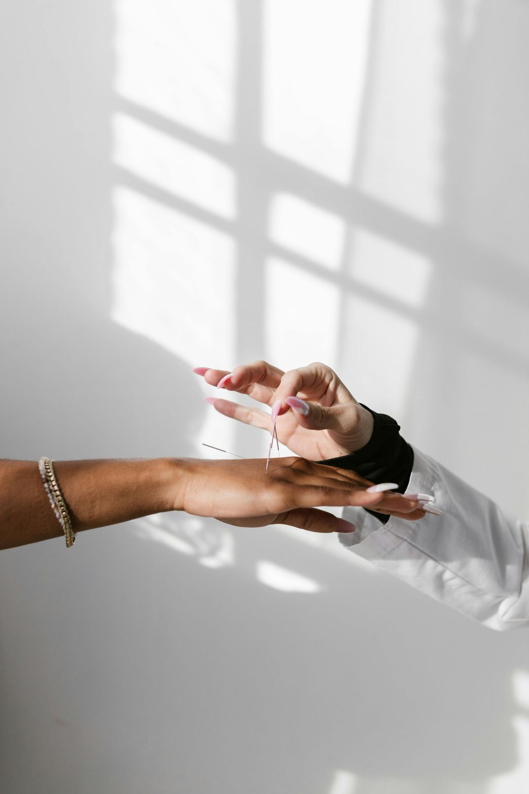 Hands exchanging a small object through a white cuff on a bright window-lit wall