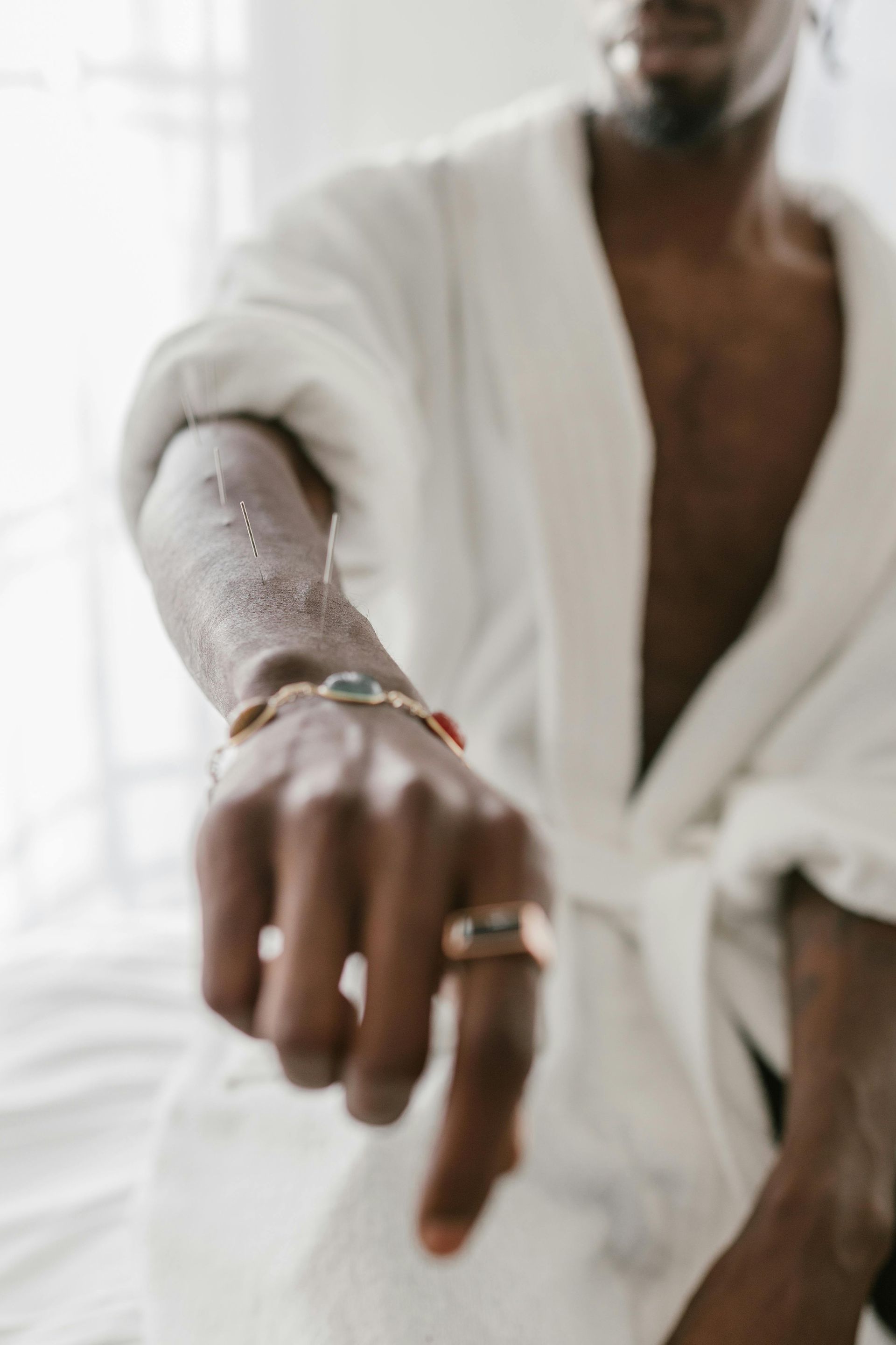 Person in a white robe extending a hand with rings in a bright indoor setting