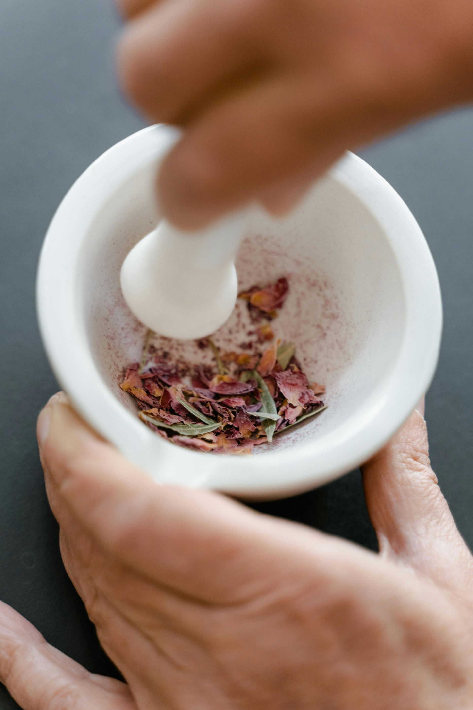 Hands grinding dried herbs in a white mortar and pestle