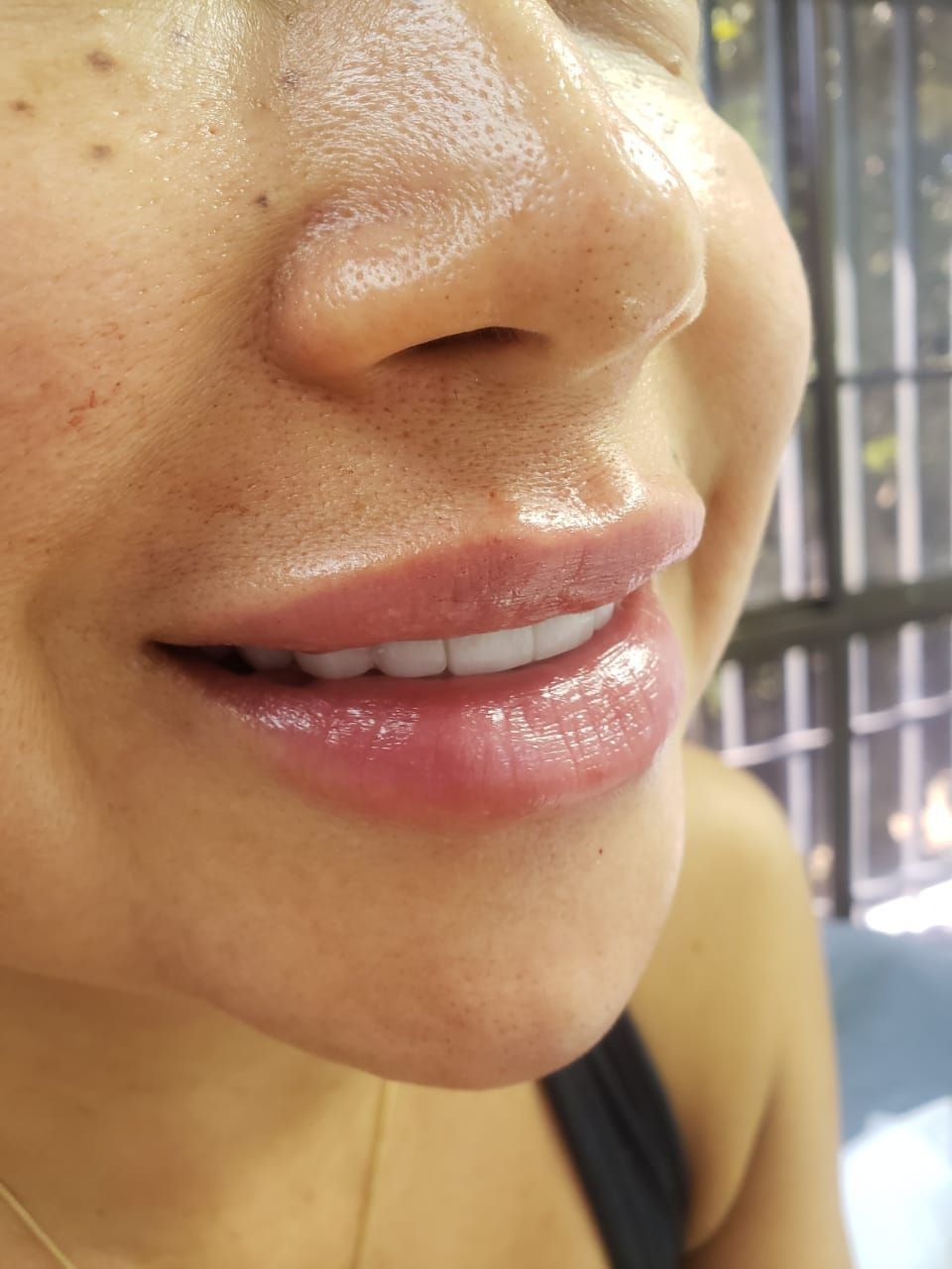 Mujer sonriendo, luciendo labios brillantes. Primer plano, interior, luz natural.