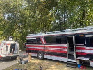 RV with red and white stripes parked outdoors with a smaller utility vehicle nearby.